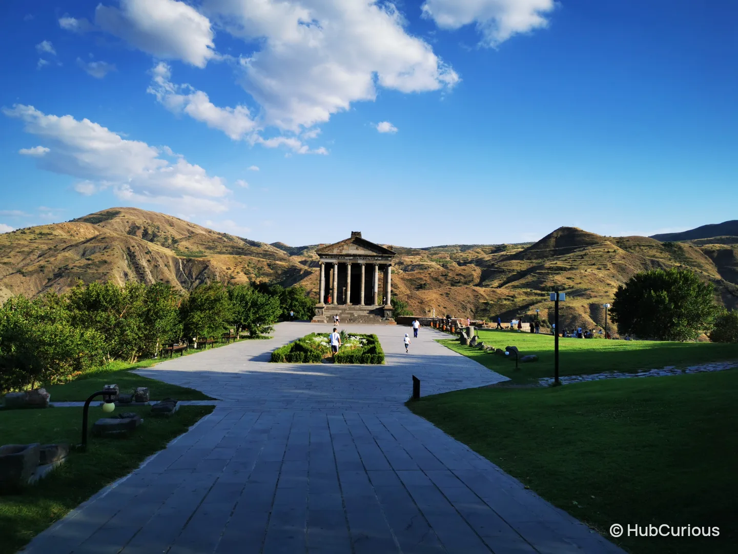 Wide paved path leading to the colonnaded Garni temple, with green lawns on either side and bare hills behind