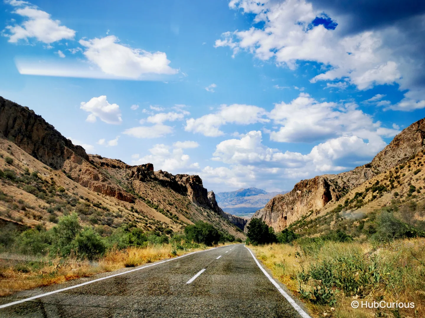 Empty two-lane road running through a dry rocky canyon in southern Armenia under a blue sky