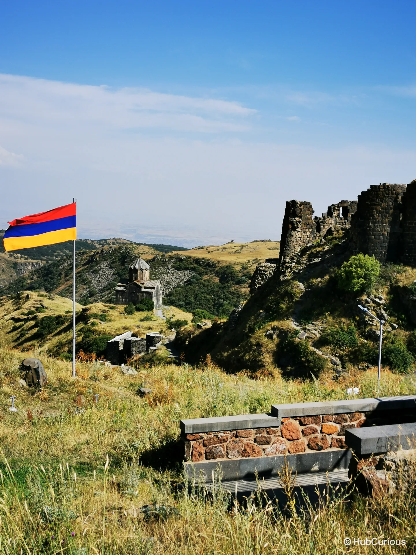 Armenian flag flying beside the ruined walls of Amberd fortress, with the Vahramashen church on the grass slope below