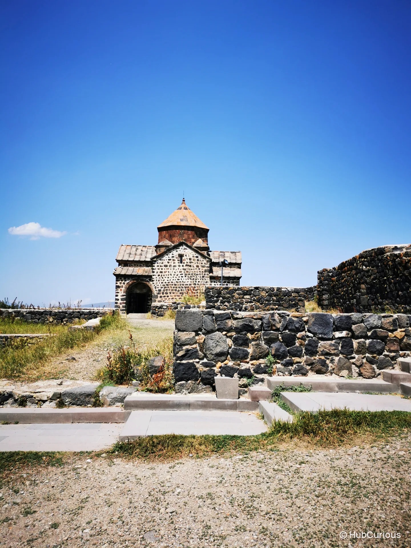 Dark stone church of Sevanavank with its red-tiled dome under a cloudless blue sky