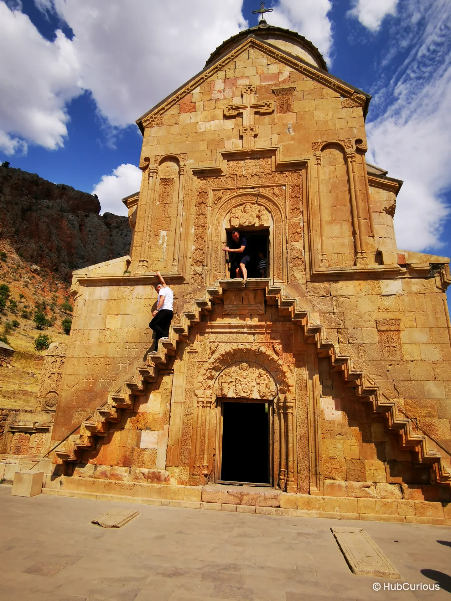 The narrow cantilevered stairs on the carved facade of Surb Astvatsatsin at Noravank, with visitors climbing to the upper doorway