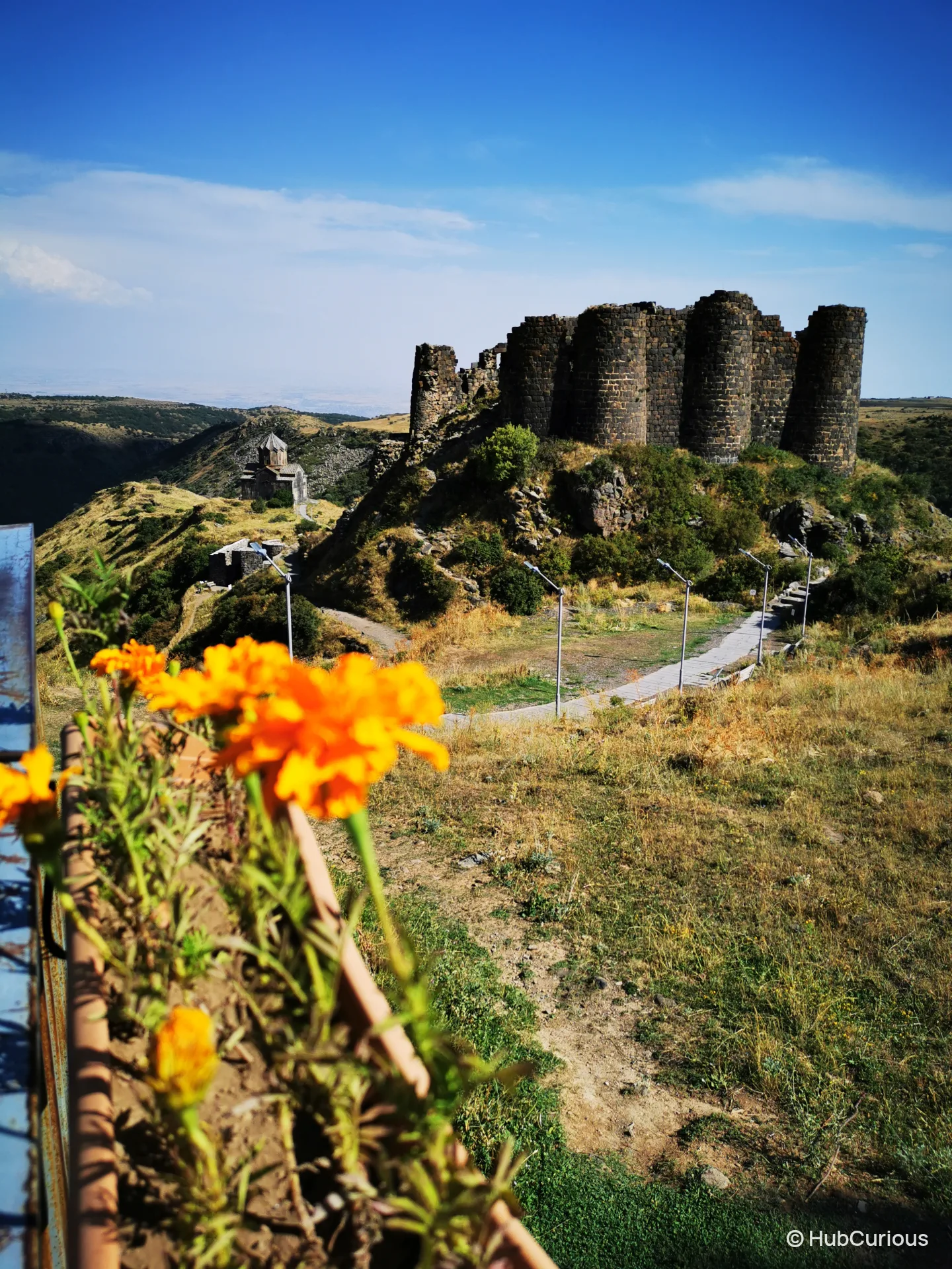 Round towers of Amberd fortress above the slope, with the Vahramashen church to the left and orange marigolds in front