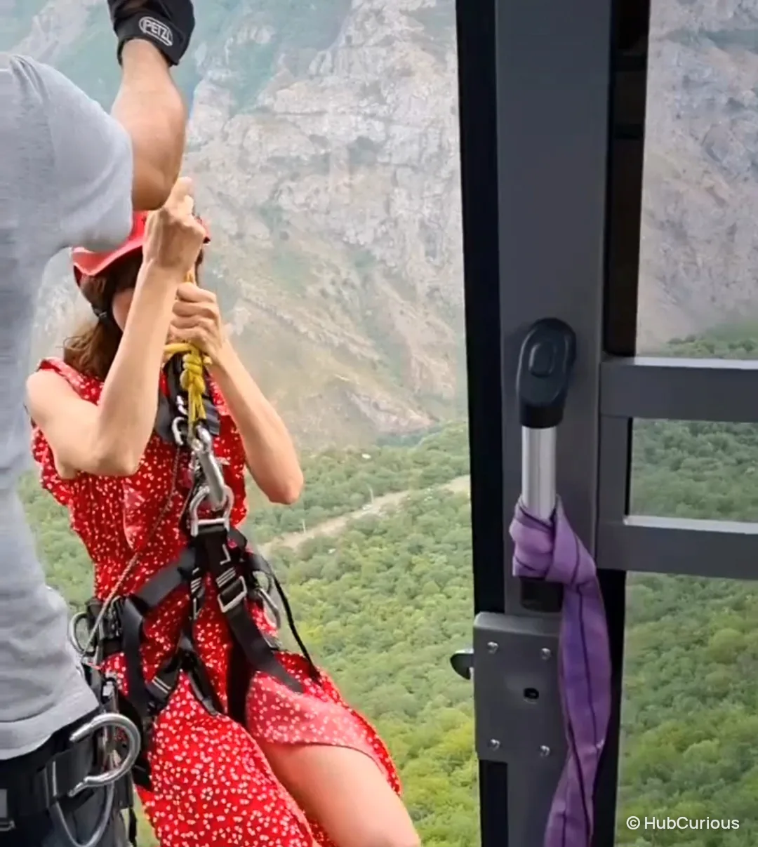 Woman in a red helmet and climbing harness holding a rope in the open door of the cable car cabin during the evacuation, the gorge far below