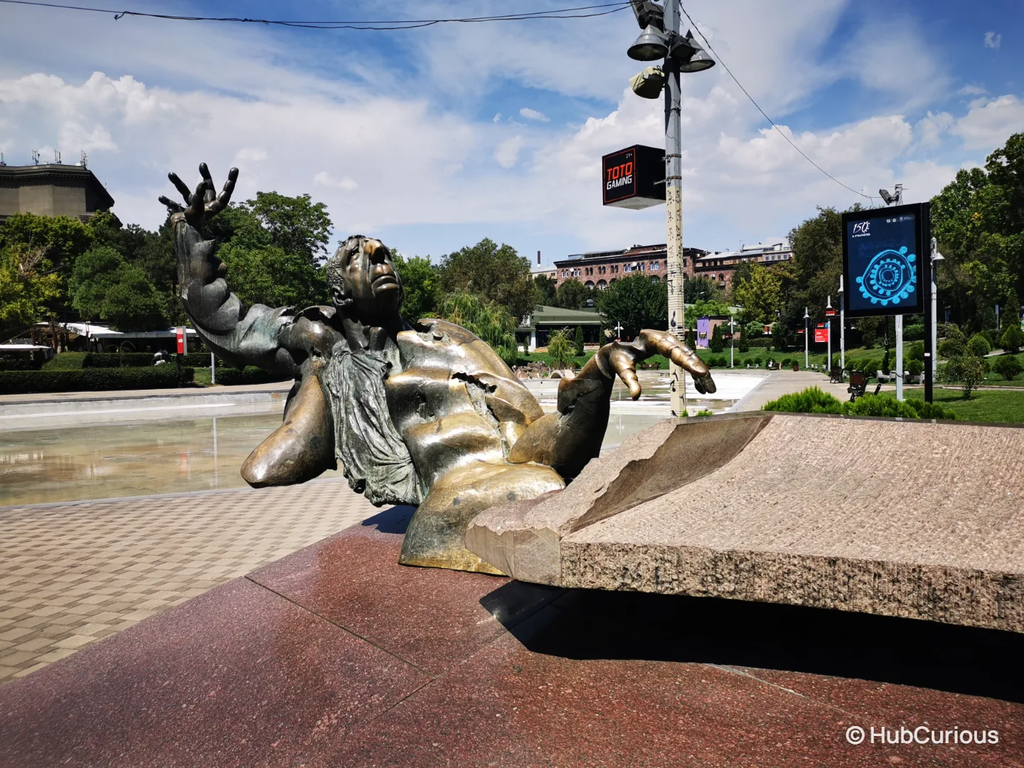 Bronze statue of composer Arno Babajanyan leaning back at a granite piano with one hand raised, by Swan Lake in Yerevan