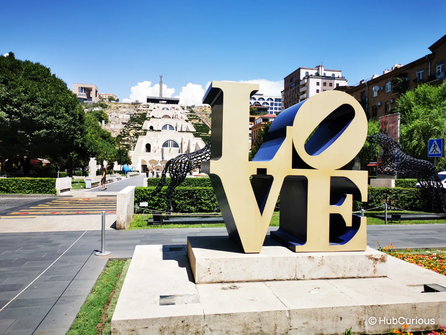Robert Indiana's gold and blue LOVE sculpture in the Cafesjian Sculpture Garden, with the Cascade rising behind it in Yerevan
