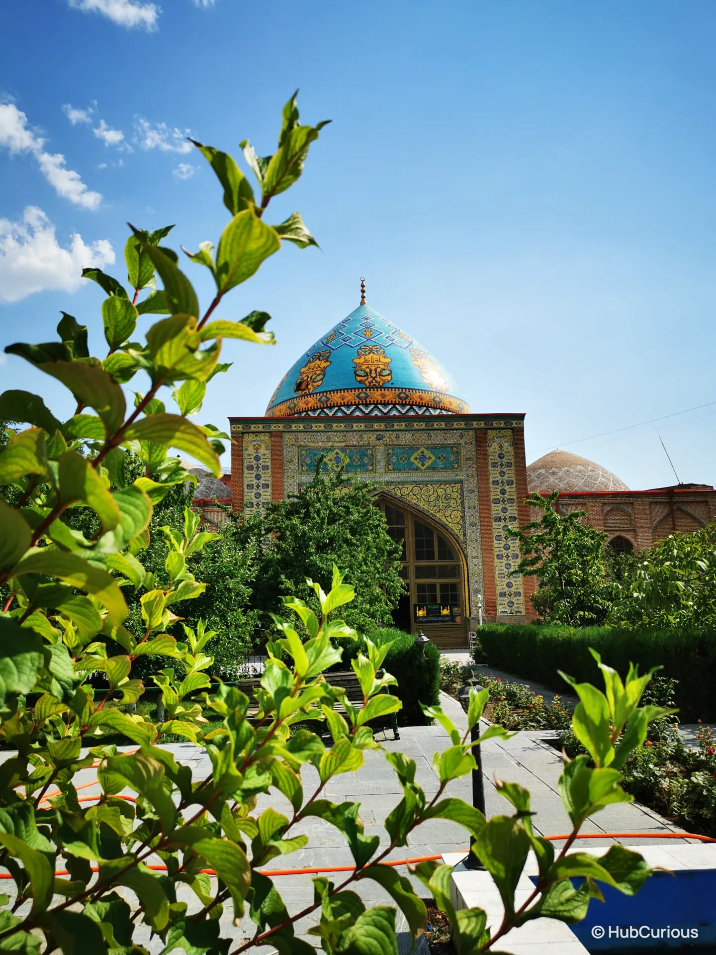 Turquoise tiled dome and patterned entrance of the Blue Mosque in Yerevan, seen through green leaves from the courtyard garden